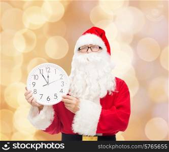christmas, holidays and people concept - man in costume of santa claus with clock showing twelve over beige lights background