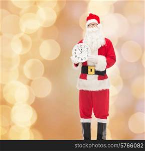 christmas, holidays and people concept - man in costume of santa claus with clock showing twelve over beige lights background