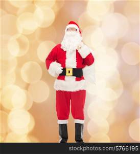 christmas, holidays and people concept - man in costume of santa claus with bag over beige lights background