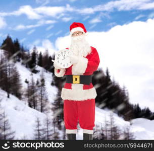 christmas, holidays and people concept - man in costume of santa claus with clock showing twelve pointing finger over snowy mountains background