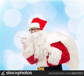 christmas, holidays and people concept - man in costume of santa claus with bag pointing finger over blue lights background