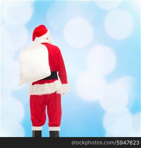 christmas, holidays and people concept - man in costume of santa claus with bag from back over blue lights background