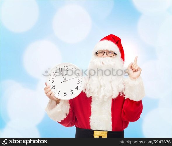 christmas, holidays and people concept - man in costume of santa claus with clock showing twelve pointing finger up over blue lights background