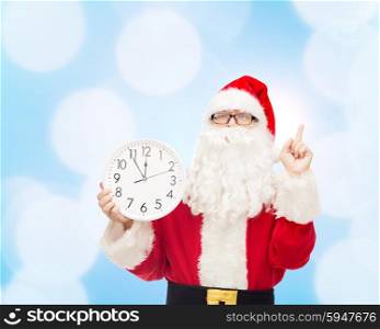 christmas, holidays and people concept - man in costume of santa claus with clock showing twelve pointing finger up over blue lights background