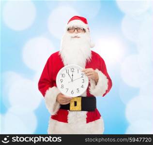 christmas, holidays and people concept - man in costume of santa claus with clock showing twelve pointing finger over blue lights background