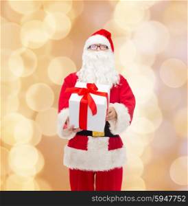 christmas, holidays and people concept - man in costume of santa claus with gift box over beige lights background
