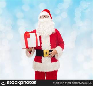 christmas, holidays and people concept - man in costume of santa claus with gift box over blue lights background