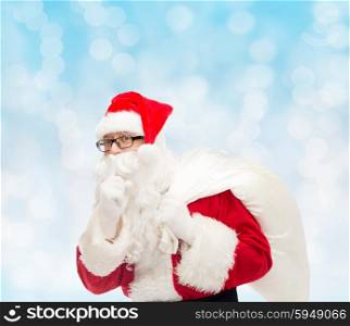 christmas, holidays and people concept - man in costume of santa claus with bag making hush gesture over blue lights background