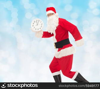 christmas, holidays and people concept - man in costume of santa claus running with clock showing twelve over blue lights background