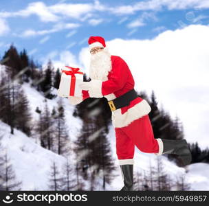 christmas, holidays and people concept - man in costume of santa claus running with gift box over snowy mountains background