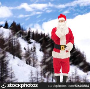 christmas, holidays and people concept - man in costume of santa claus making hush gesture over snowy mountains background
