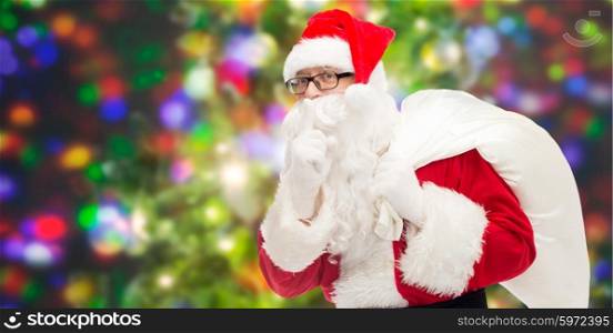 christmas, holidays and people concept - man in costume of santa claus with bag making hush gesture over party lights background