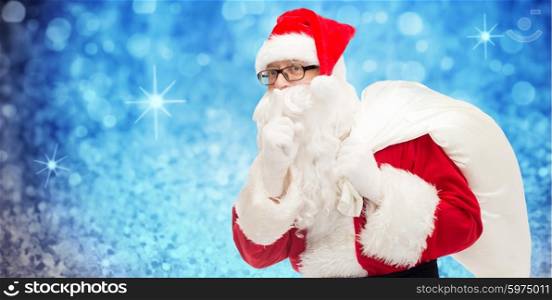 christmas, holidays and people concept - man in costume of santa claus with bag making hush gesture over blue glitter or lights background