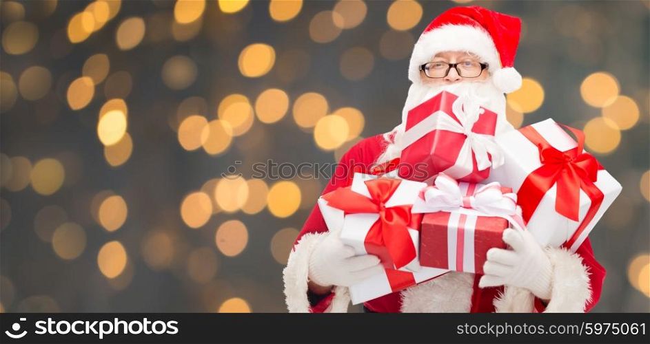christmas, holidays and people concept - man in costume of santa claus with gift boxes over golden lights background