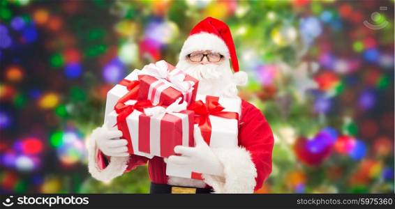 christmas, holidays and people concept - man in costume of santa claus with gift boxes over party lights background