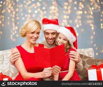 christmas, holidays and people concept - smiling family in santa helper hats with many gift boxes reading postcard over lights background