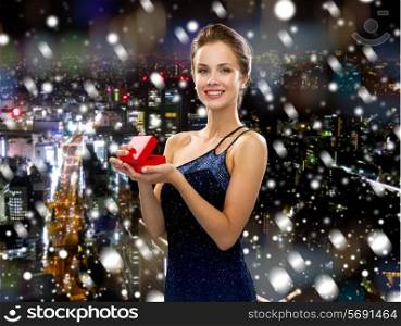 christmas, holidays and people concept - smiling woman in evening dress with small red gift box over snowy night city background