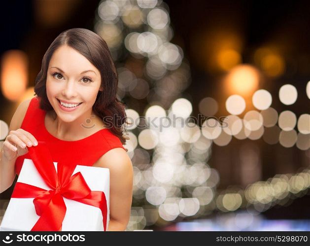 christmas, holidays and people concept - smiling woman in red dress with gift box over lights background. smiling woman in red dress with christmas gift box
