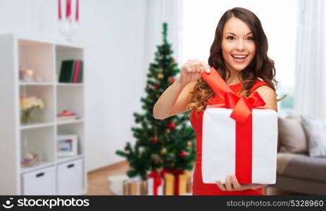 christmas, holidays and people concept - smiling woman in red dress with gift box over home room background. smiling woman with christmas gift at home