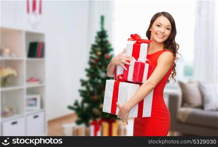 christmas, holidays and people concept - smiling woman in red dress with gift boxes over home room background. smiling woman with christmas gifts at home