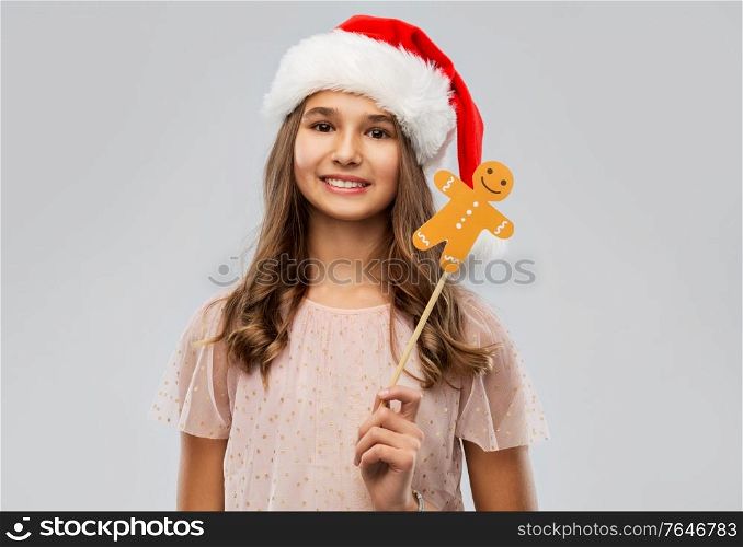 christmas, holidays and photo booth concept - happy smiling teenage girl in santa helper hat with gingerbread man party accessory over grey background. happy teenage girl in santa hat on christmas