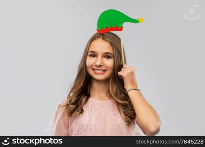 christmas, holidays and photo booth concept - happy smiling teenage girl with santa helper hat party accessory over grey background. happy teenage girl with santa helper hat accessory