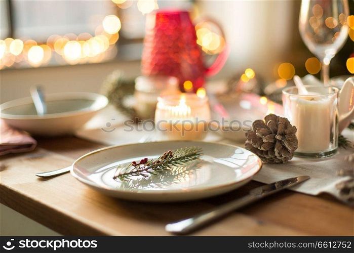 christmas, holidays and table setting concept - plate decorated with fir branch for festive dinner at home. table setting for christmas dinner at home