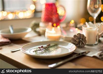 christmas, holidays and table setting concept - plate decorated with fir branch for festive dinner at home. table setting for christmas dinner at home