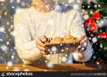 christmas, holidays, baking, people and food concept - close up of woman with oat cookies sitting at wooden table at home