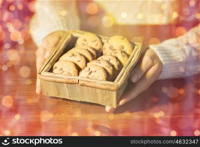 christmas, holidays, baking, people and food concept - close up of woman with oat cookies sitting at wooden table over lights