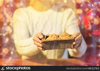 christmas, holidays, baking, people and food concept - close up of woman with oat cookies sitting at wooden table over lights