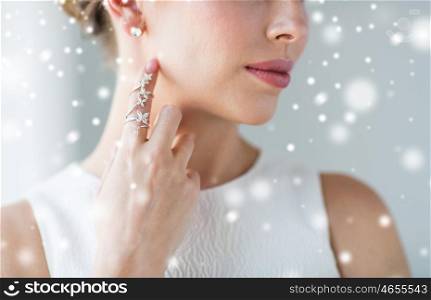 christmas, holidays, beauty, jewelry and luxury concept - close up of beautiful woman with golden ring and diamond earring over snow