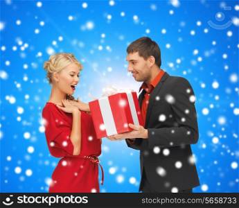 christmas, holidays, celebration and people concept - smiling man and woman with present over blue over blue snowy background