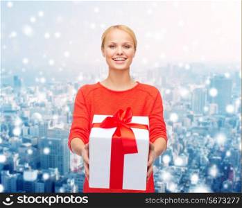 christmas, holidays, celebration and people concept - smiling woman in red clothes with gift box over over snowy city background