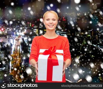 christmas, holidays, celebration and people concept - smiling woman in red clothes with gift box over over snowy night city background