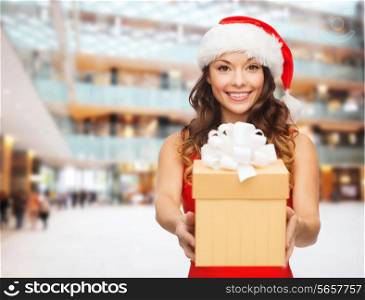 christmas, holidays, celebration and people concept - smiling woman in red dress with gift box over shopping center background