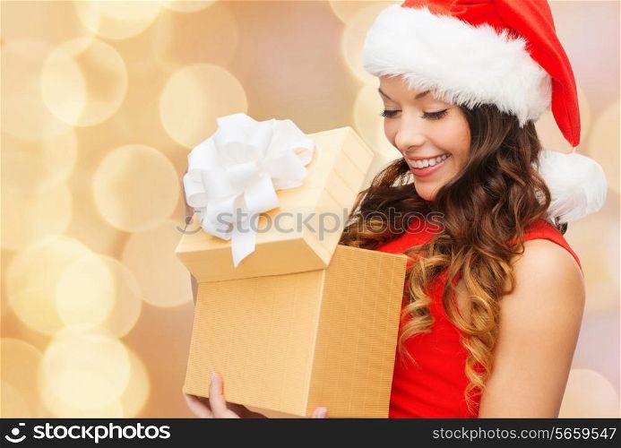 christmas, holidays, celebration and people concept - smiling woman in red dress with gift box over beige lights background