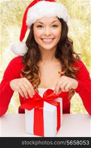 christmas, holidays, celebration and people concept - smiling woman in santa helper hat with gift box over yellow lights background
