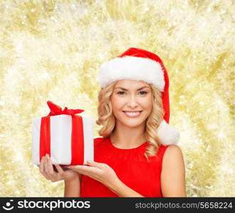 christmas, holidays, celebration and people concept - smiling woman in santa helper hat with gift box over yellow lights background