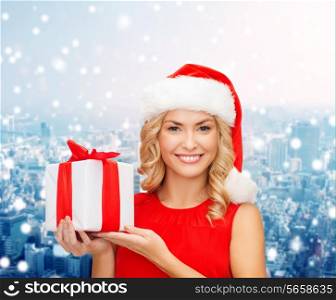 christmas, holidays, celebration and people concept - smiling woman in santa helper hat with gift box over snowy city background