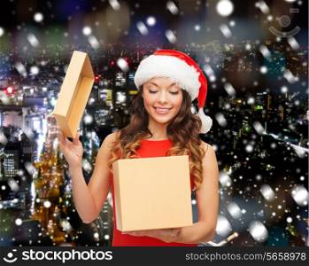 christmas, holidays, celebration and people concept - smiling woman in santa helper hat with gift box over snowy night city background