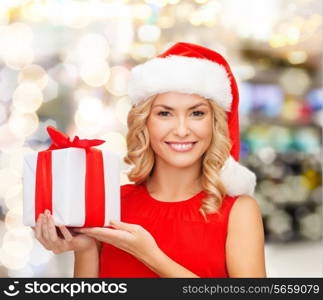 christmas, holidays, celebration and people concept - smiling woman in santa helper hat with gift box over lights background