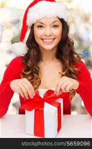 christmas, holidays, celebration and people concept - smiling woman in santa helper hat with gift box over lights background