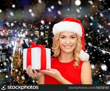christmas, holidays, celebration and people concept - smiling woman in santa helper hat with gift box over night snowy city background