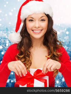 christmas, holidays, celebration and people concept - smiling woman in santa helper hat with gift box over blue snowy background