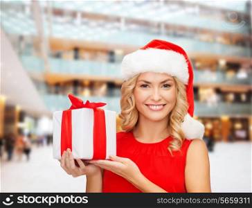 christmas, holidays, celebration and people concept - smiling woman in santa helper hat with gift box over shopping center background