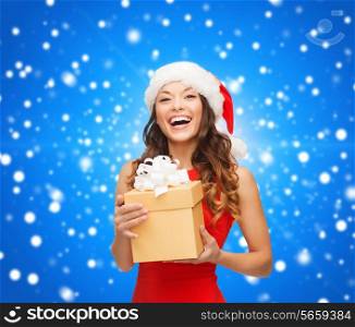 christmas, holidays, celebration and people concept - smiling woman in santa helper hat with gift box over blue snowing background