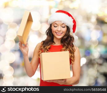 christmas, holidays, celebration and people concept - smiling woman in santa helper hat with gift box over lights background