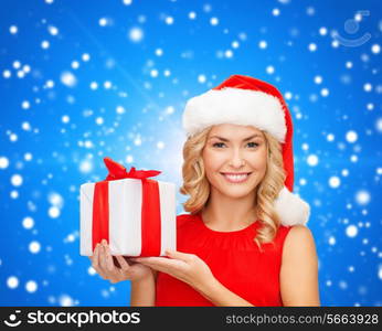 christmas, holidays, celebration and people concept - smiling woman in santa helper hat with gift box over blue snowing background