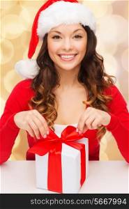 christmas, holidays, celebration and people concept - smiling woman in santa helper hat with gift box over beige lights background